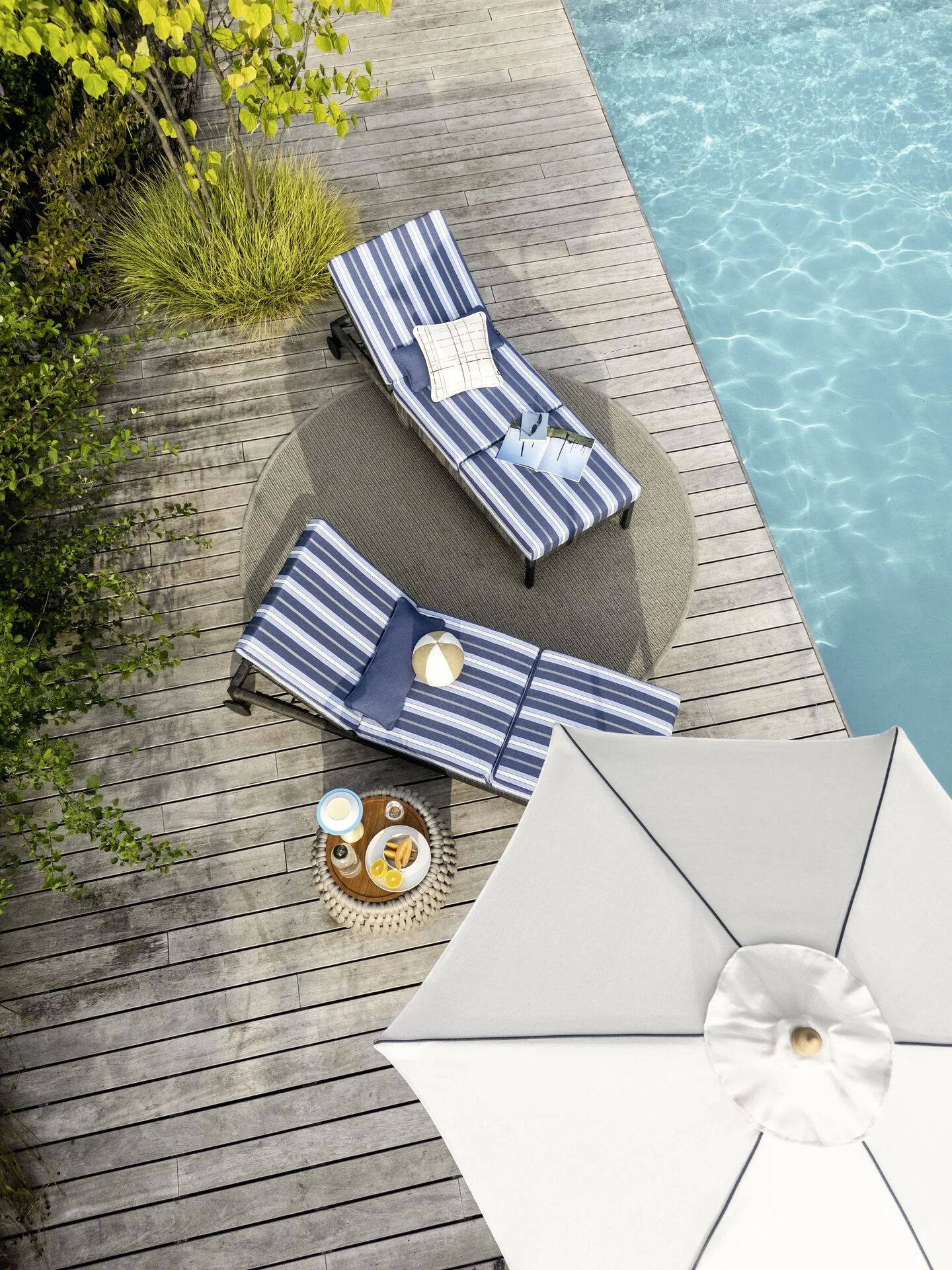 Outdoor ligbedden met blauw-witte gestreepte stoffering naast een zwembad