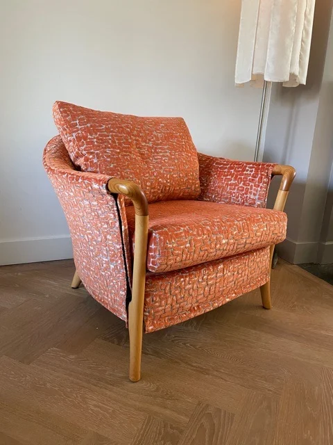 Oranje retro fauteuil met houten armleuningen op een eiken vloer