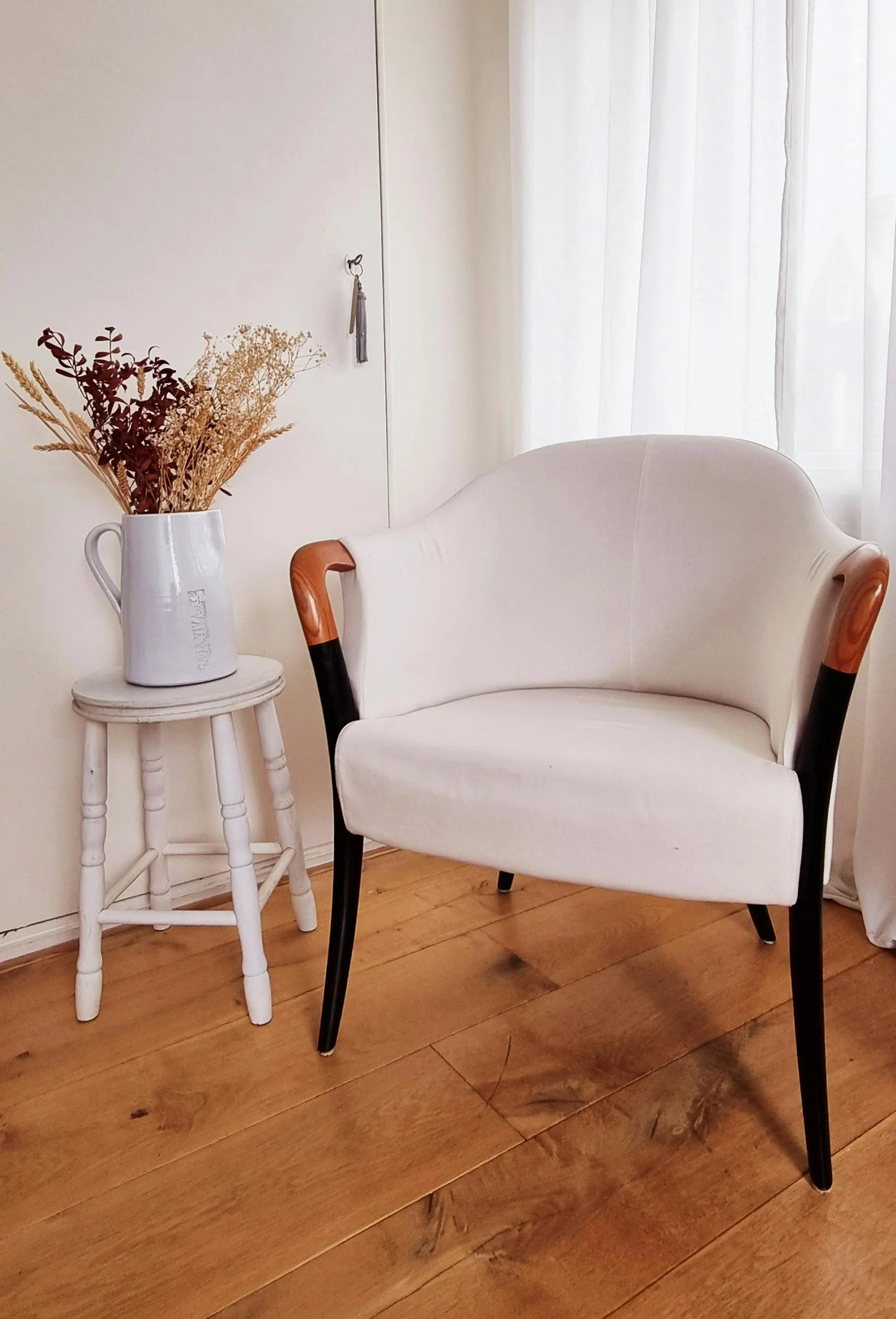 Opnieuw gestoffeerde crème fauteuil met cognackleurige houten armdetails in een licht interieur