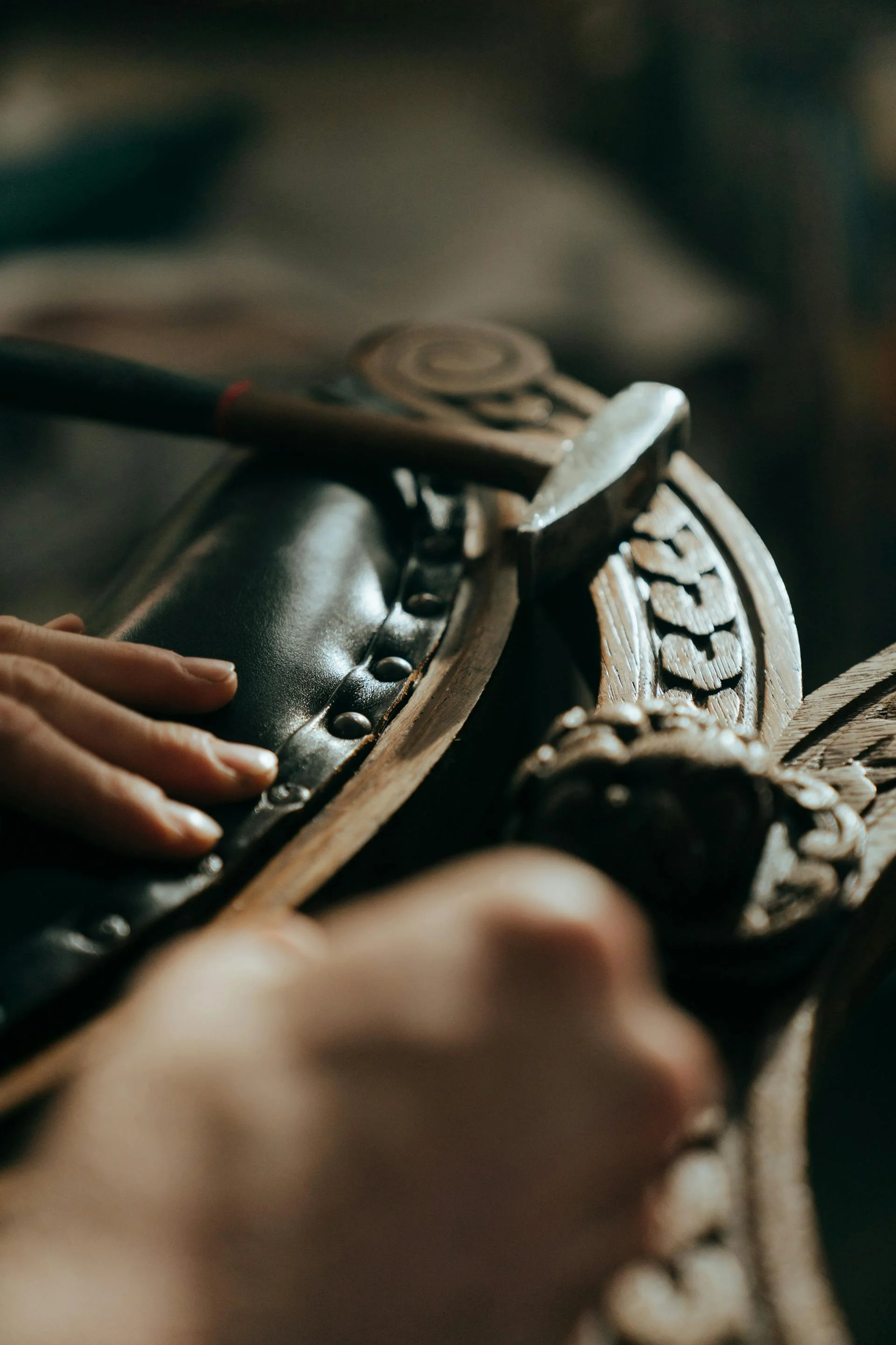 Stoffeerder zet met de hand sierspijkers in een gesneden houten frame van een antiek meubel — restyling van een bijzonder stuk
