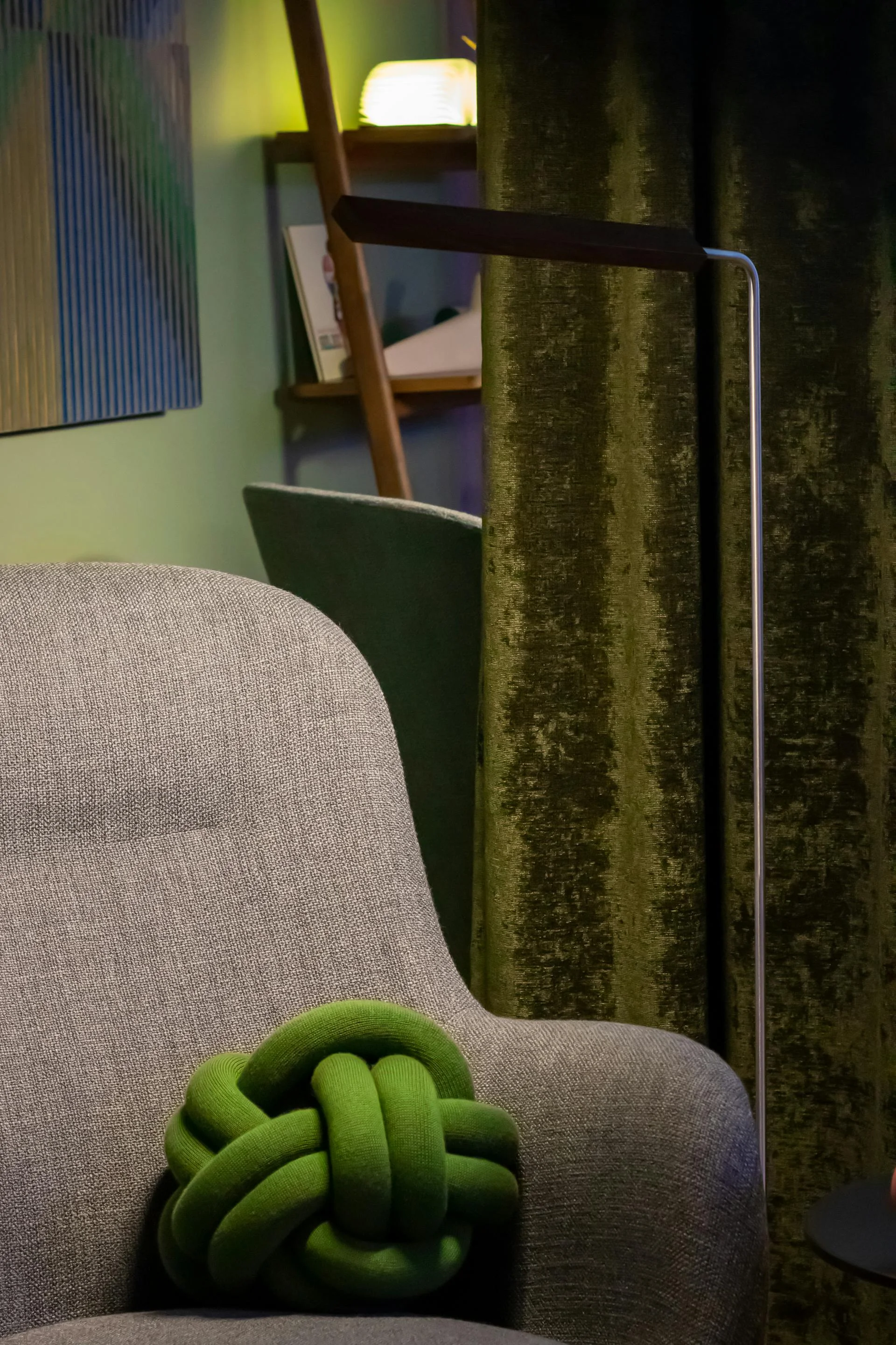 Grijze gestoffeerde fauteuil met groen knoopkussen in een moody atelier — voorbeeld van een restyling-project