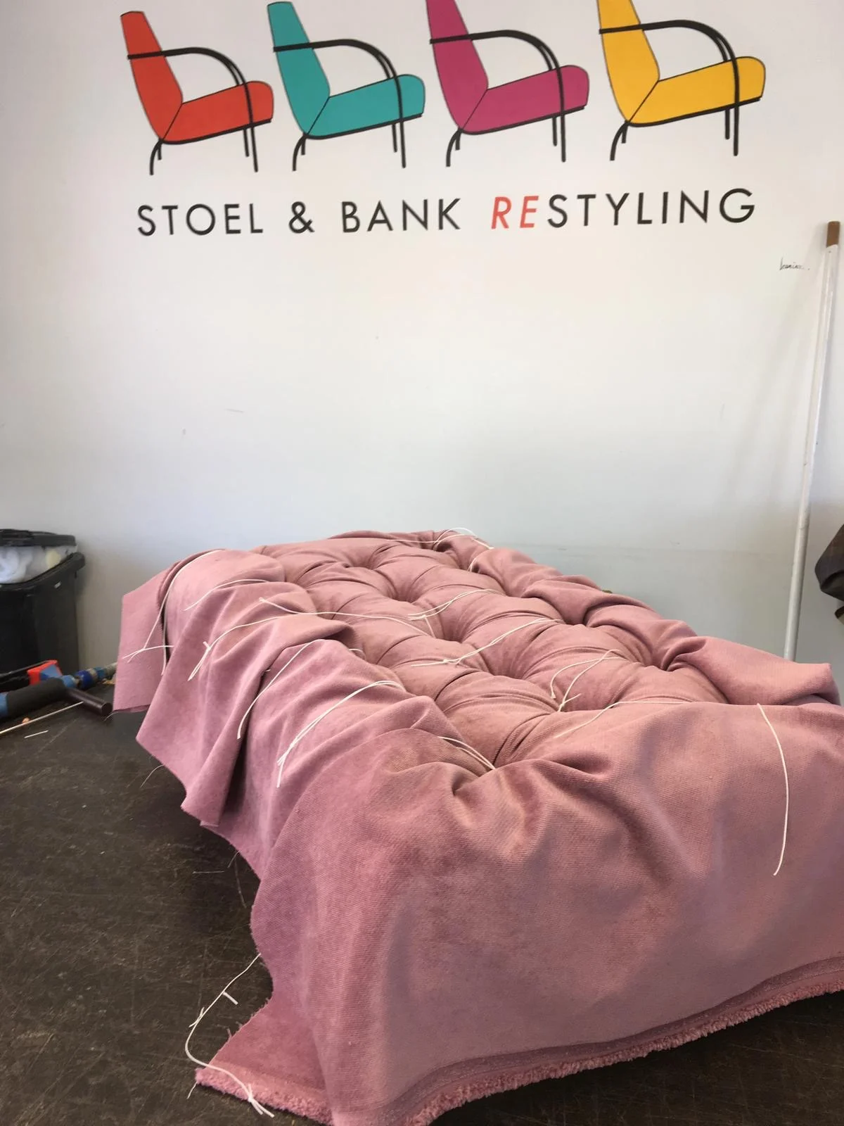 Bank in capitonnage-afwerking op de werkvloer van Stoel & Bank Restyling in Grootebroek, onder het bedrijfslogo